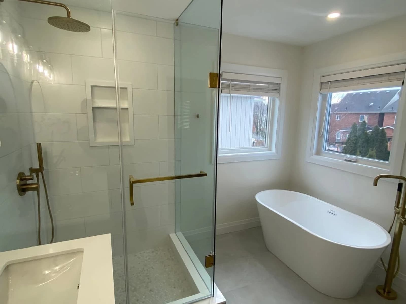 Bathroom with a freestanding tub, glass shower, white wall tile, window, and brass shower hardware