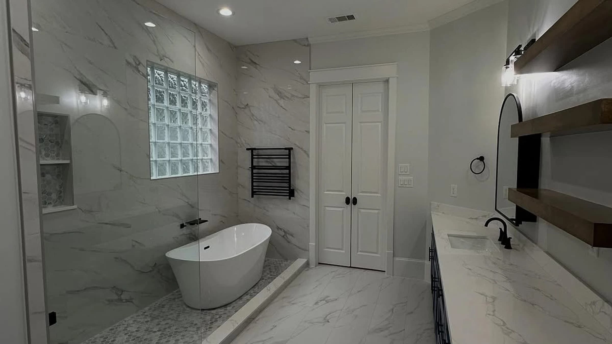 Finished bathroom remodel by Pioneer Construction with freestanding tub, glass shower, blue vanity, and marble-look tile