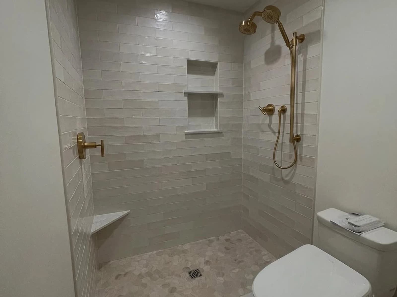 Walk-in custom shower with light tile walls, gold fixtures, built-in niche, and open entry