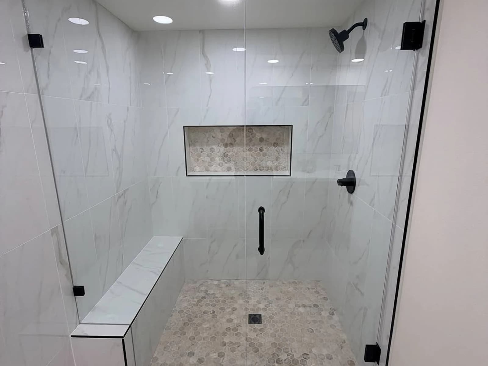 Marble-look tile shower with glass enclosure, bench, recessed niche, and black shower hardware