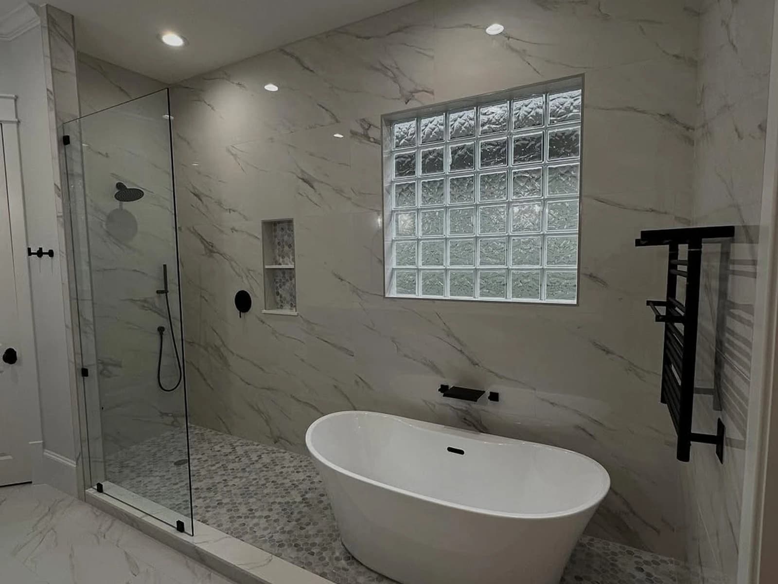 Finished bathroom with a freestanding tub, glass shower, glass block window, and marble-look tile