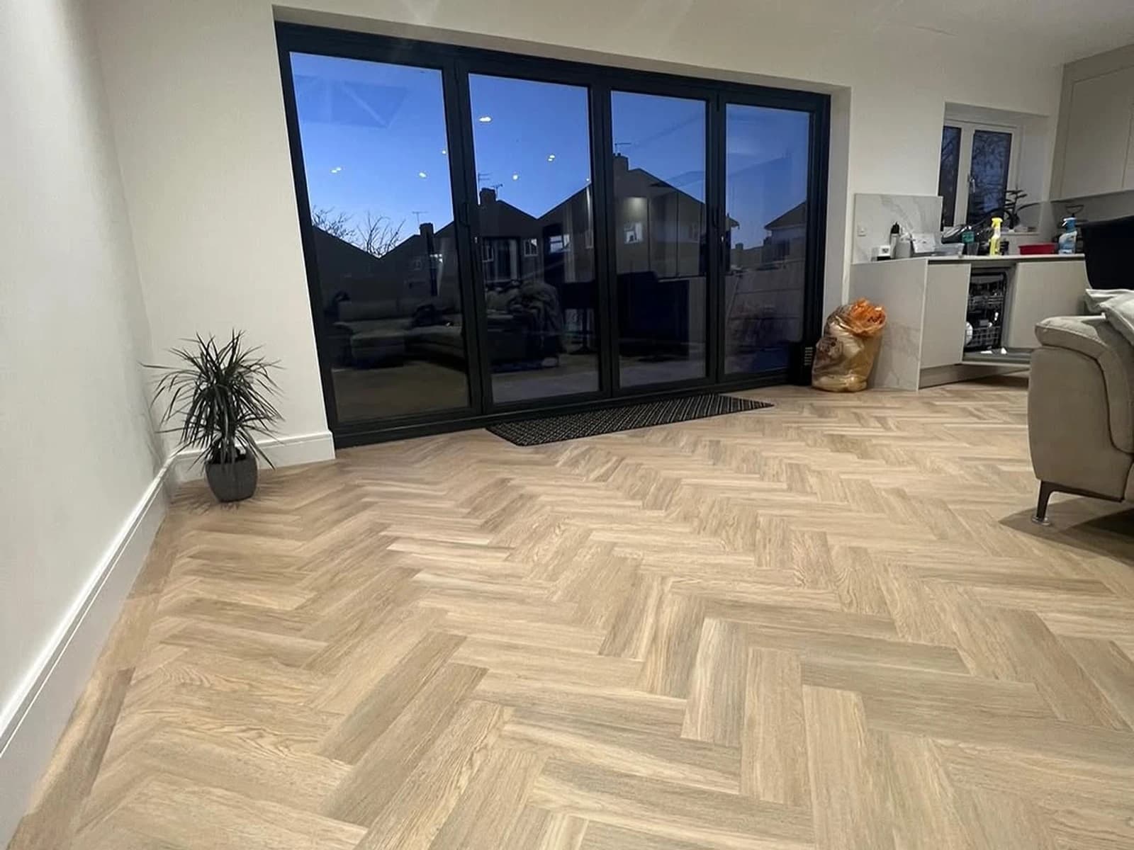 Living room flooring installation with light herringbone wood-look planks and black patio doors