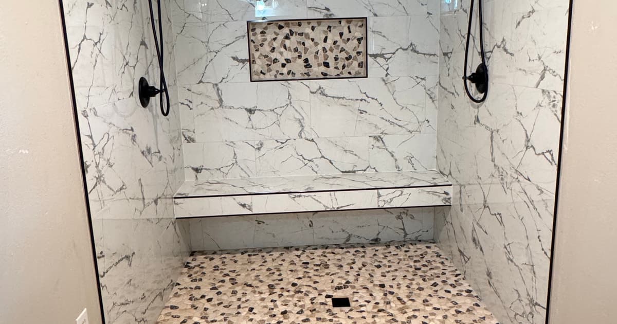 Curbless custom shower with a full-width bench, mosaic niche, dual black fixtures, and mixed-tone mosaic floor in Marshall TX